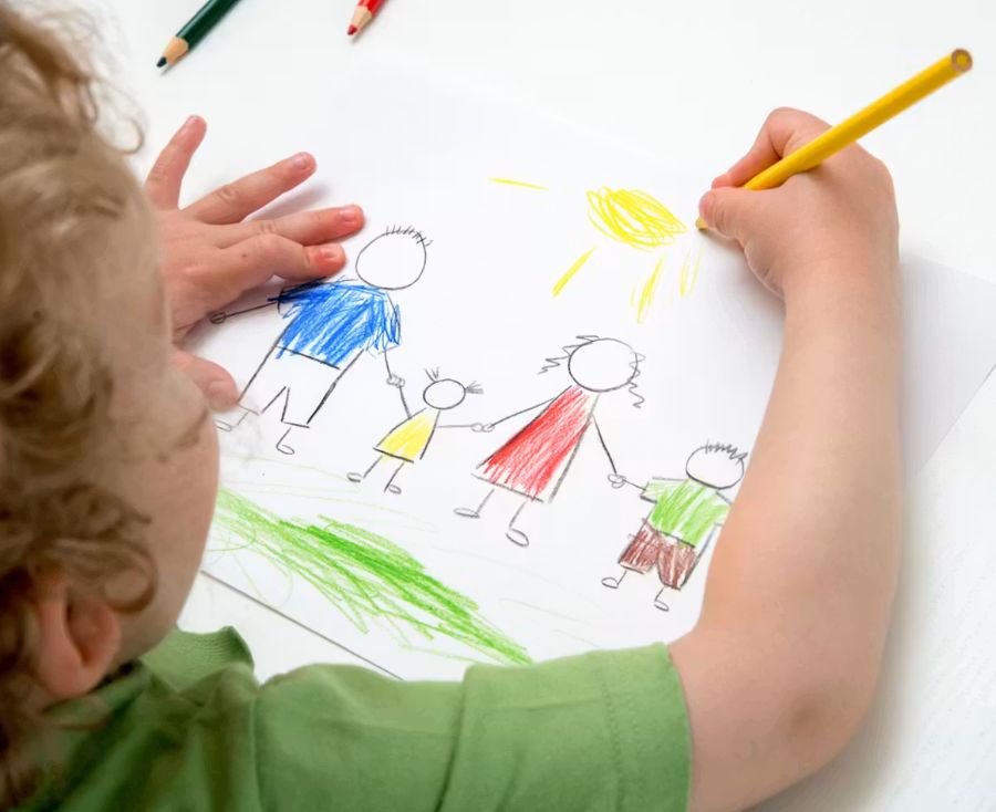 A child drawing a picture of their family with coloured pencils